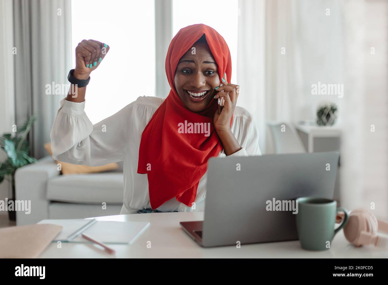 Neue Jobmöglichkeit. Überglücklich afroamerikanische muslimische Frau, die am Handy spricht und Erfolg feiert Stockfoto