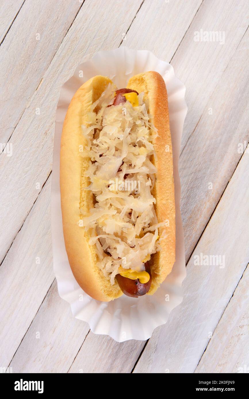 Aufnahme eines Kraut-Hundes in einem hohen Winkel. Ein gegrillter Hot Dog auf einem Brötchen mit Senf und Sauerkraut auf einem rustikalen Picknicktisch aus weißem Holz. Stockfoto