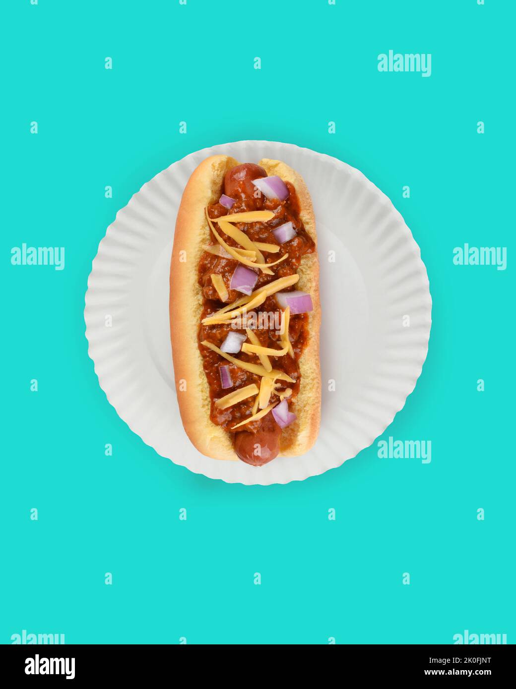 Flach Lay Hot Dog in Bun Still Life. Fankfurter in Brötchen mit Chili, Käse und Zwiebeln auf einem weißen Papierteller auf blauem Hintergrund mit Kopierfläche. Stockfoto
