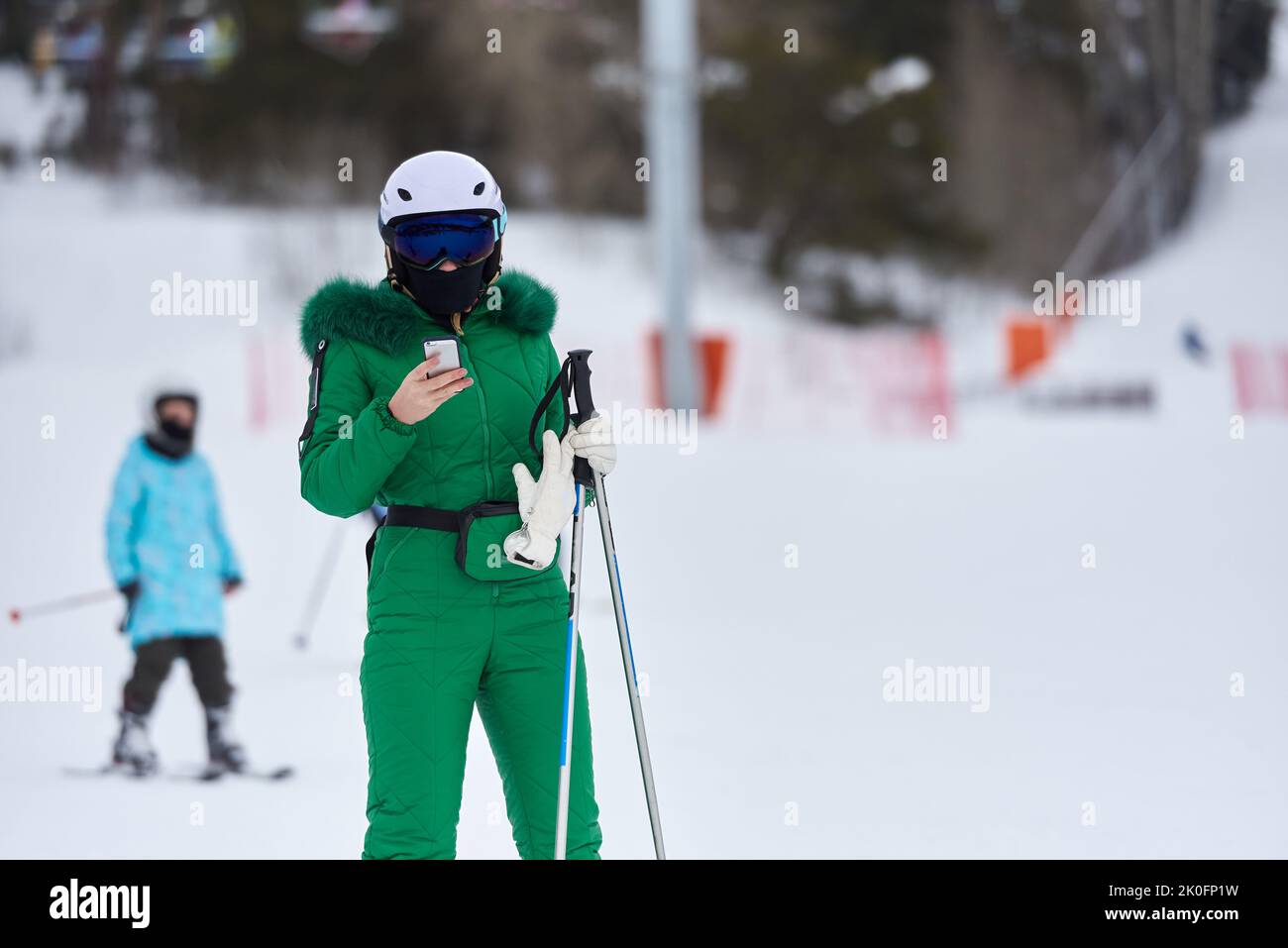 Frau Skifahrerin im grünen Skianzug Blick auf Smartphone. Stockfoto