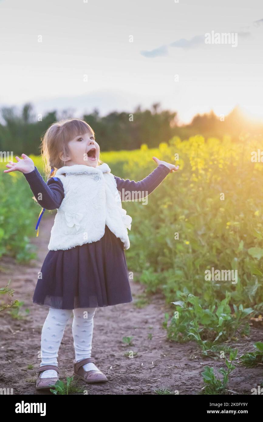 Ein Kind mit ukrainischen Bändern im Haar singt auf einem blühenden Feld Stockfoto