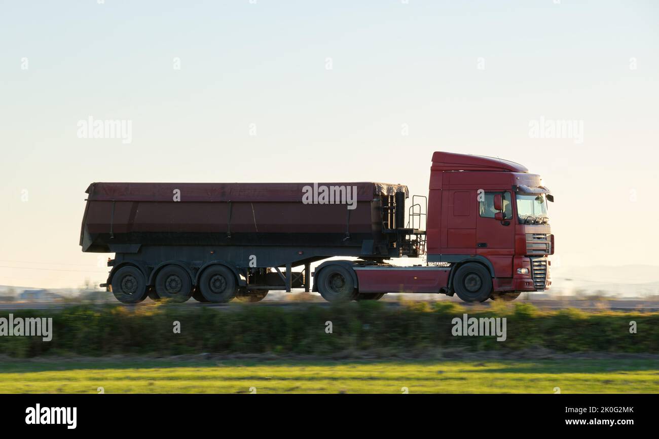 Sattelschlepper mit Kipplastwagen, der Sand aus dem Steinbruch transportiert und auf der Autobahn unterwegs ist, um am Abend Güter zu schleppen. Liefertransport und Logistik Stockfoto