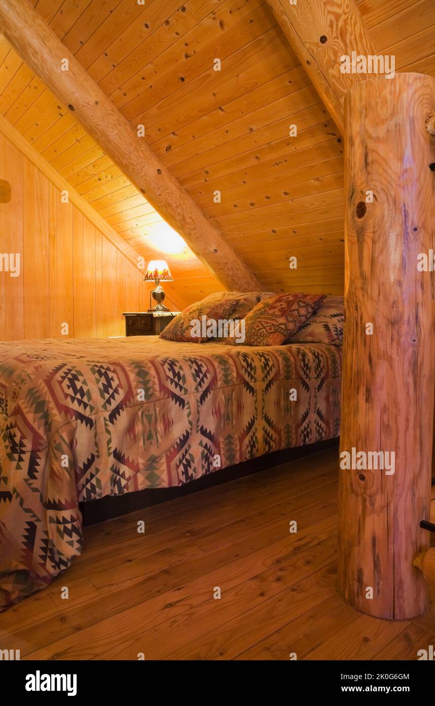 Queen-Size-Bett mit Navajo gemusterter Bettdecke im Gästeschlafzimmer auf der oberen Ebene im skandinavischen Blockhaus-Stil. Stockfoto