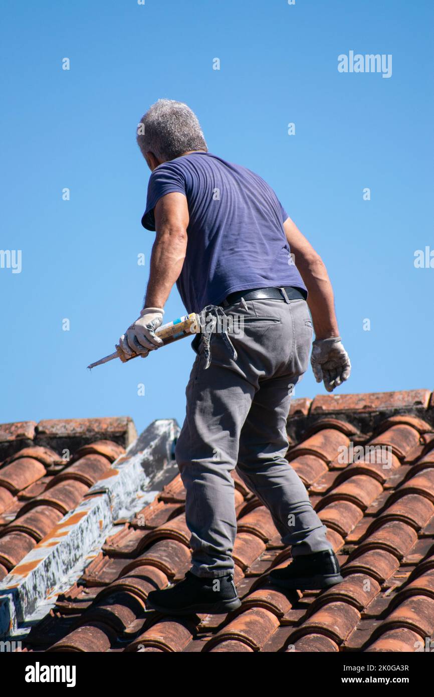 Mann, der Dachziegel zur Vorbereitung auf Stürme und Hurrikane befestigt. Winterwinde, die Reparaturen an Dachziegeln im Außenbereich erforderlich machen. Stockfoto