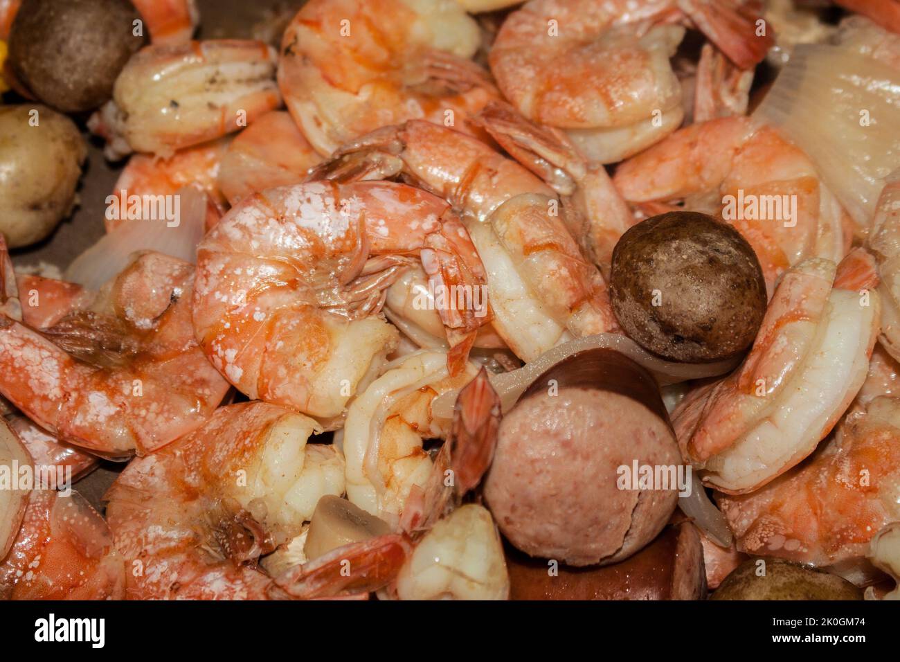 Köstliche gekochte Garnelen umgeben von Würstchen und Pilzen und Zwiebeln in Meeresfrüchten kochen - selektiver Fokus Stockfoto