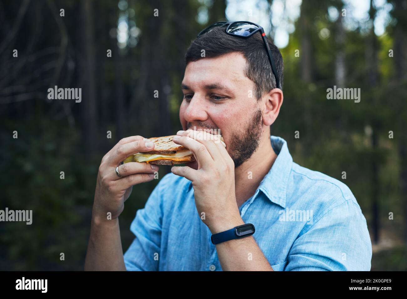 Ein junger Mann isst ein Sandwich in der Natur. Vorderansicht. Stockfoto