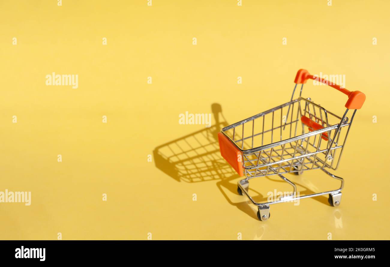 Kleiner Supermarkt Lebensmittelgeschäft Push Cart zum Einkaufen. Shopaholic. Käufer. Einkaufskonzept. Nahaufnahme. Isolierter Einkaufswagen auf gelbem Hintergrund. Cop Stockfoto