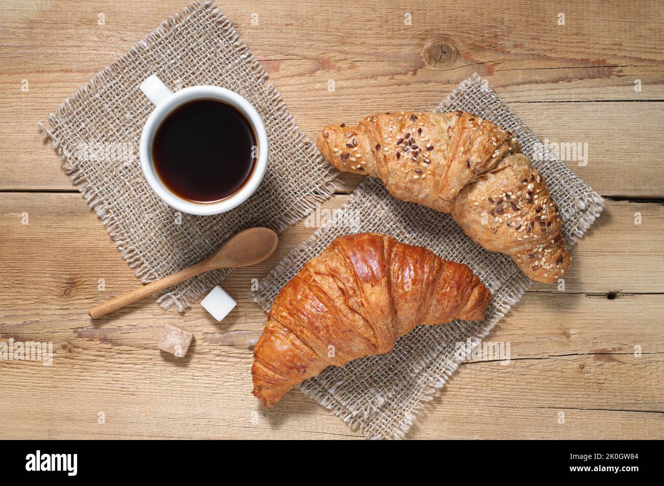 Zwei verschiedene Croissants und eine Tasse Kaffee zum Frühstück auf einem Holztisch. Draufsicht Stockfoto