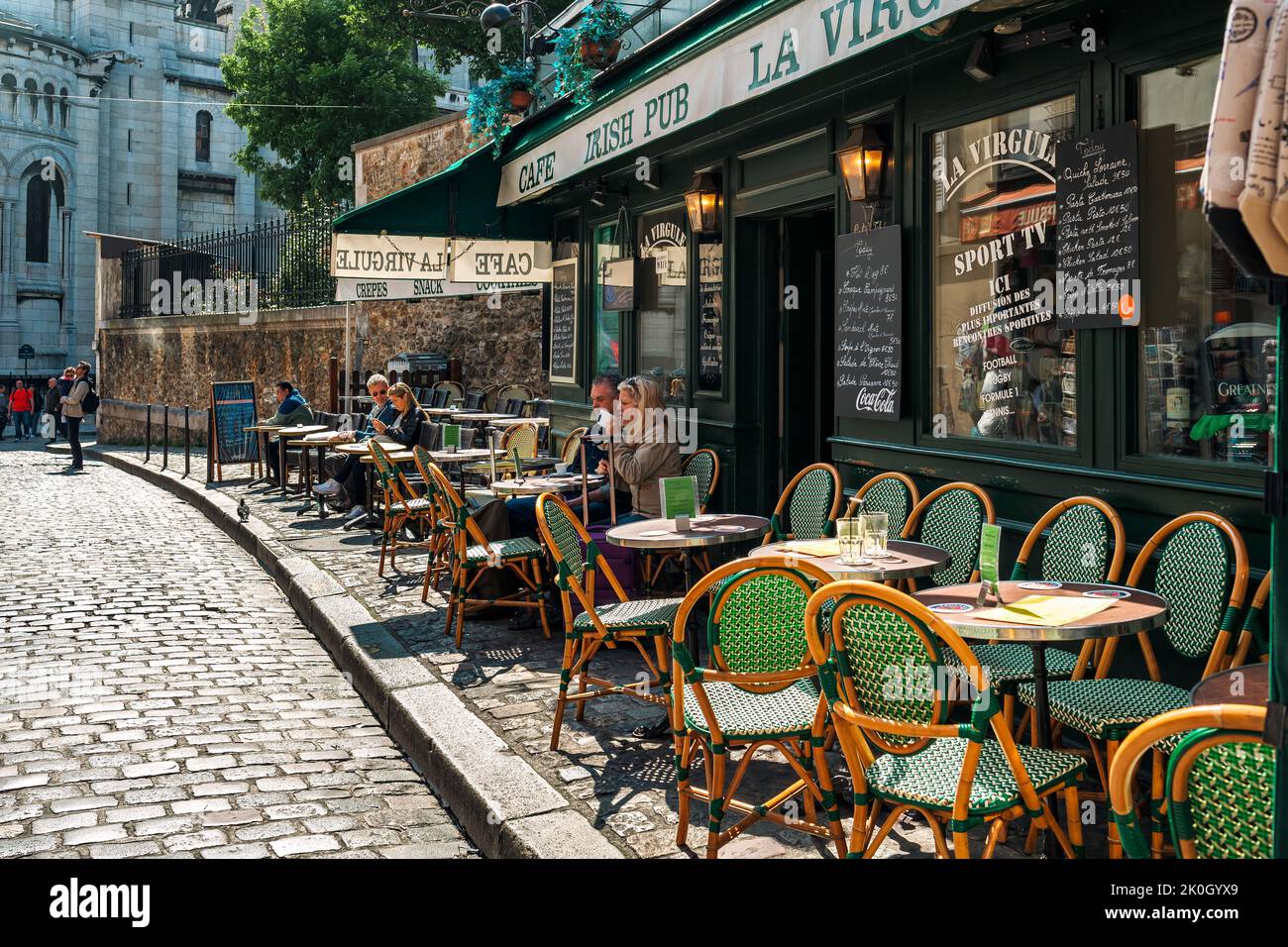 Menschen, die Kaffee trinken, werden in einem typischen Café im Freien mit alten Stühlen und Tischen auf dem Bürgersteig der gepflasterten Straße in Paris, Frankreich, serviert. Stockfoto