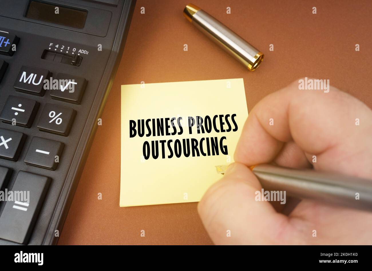 Geschäftskonzept. Ein Rechner liegt auf einer braunen Oberfläche, eine Hand mit einem Stift macht eine Beschriftung auf einem Aufkleber - Business Process Outsourcing Stockfoto
