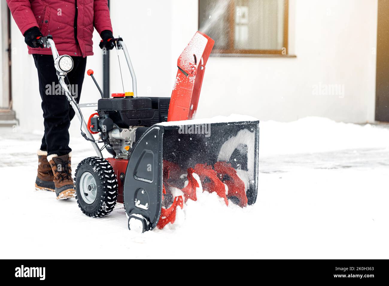 Nahaufnahme des roten Schneefräsers in Aktion. Älterer älterer Mann im Freien vor dem Haus, der Schneefräsmaschine zum Entfernen von Schnee auf dem Hof verwendet. Schneefräse im Winter vor dem Haus. Junger Arbeiter, der Schnee bläst Stockfoto