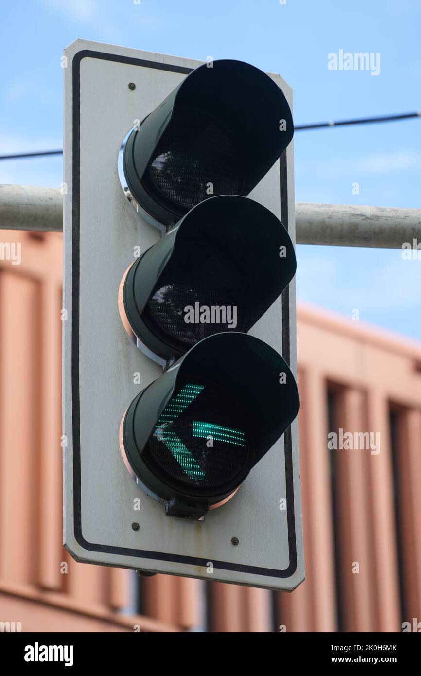 Nahaufnahme einer Ampel, die an einem sonnigen Tag ein grünes Licht für Autos zeigt, die links von der Straße abbiegen Stockfoto