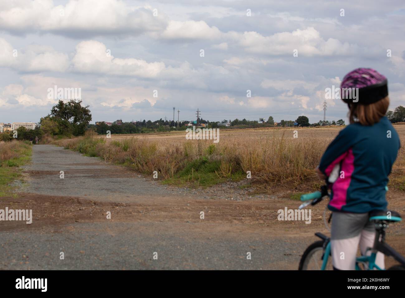 Ein kleines Mädchen auf ihrem Fahrrad und hielt an und schaut auf die Landschaft vor ihr. Die Wolken sind graublau und bedrohlich. Das helmeted Kind ist zurück Stockfoto