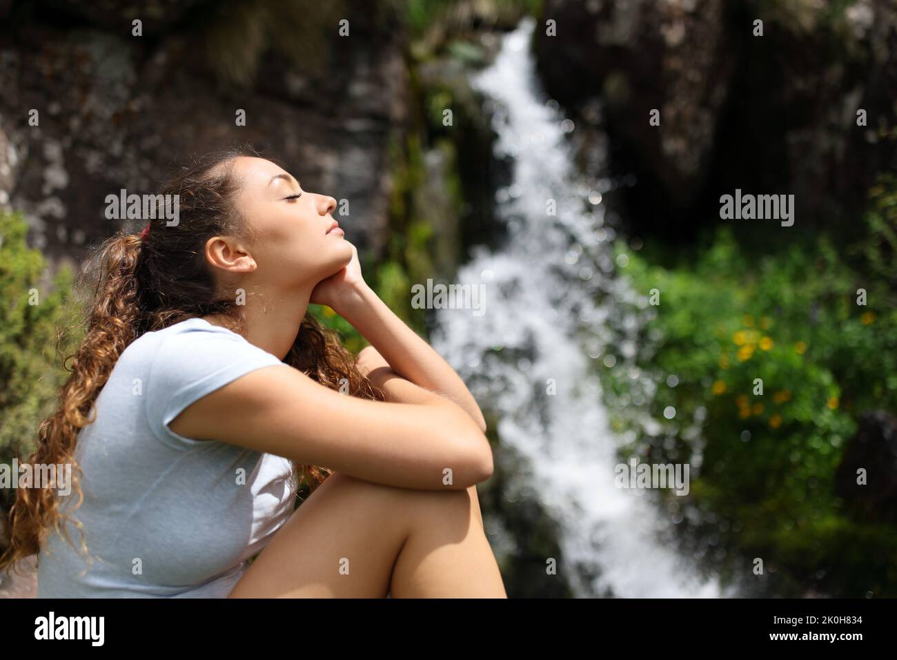 Seitenansicht Porträt einer Frau, die sich in einem kleinen Wasserfall im Berg entspannt Stockfoto