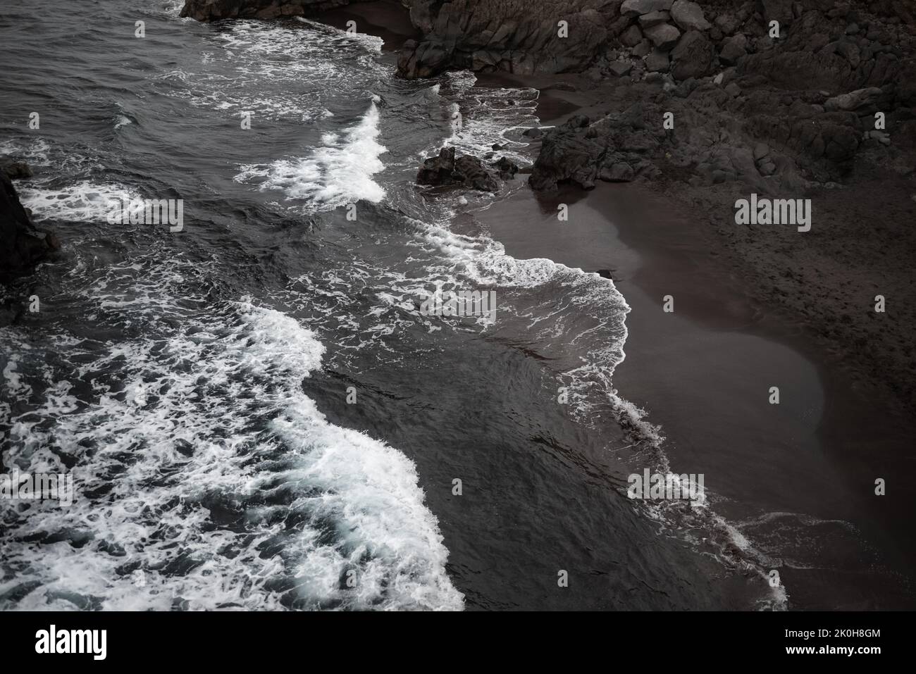 Luftaufnahme des schwarzen Sandstrandes. Kleine vulkanische Gesteine und grafische diagonale Wellen Stockfoto