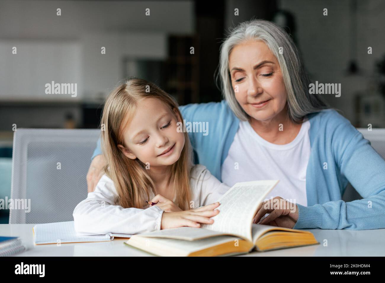 Lächelndes, konzentriertes, intelligentes europäisches kleines Mädchen mit pensionierter Großmutter liest Buch, genießt das Studium Stockfoto