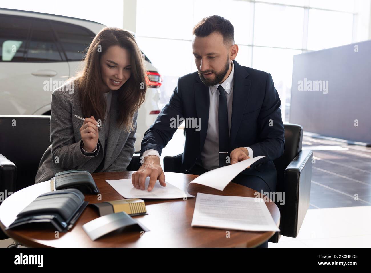 Junge Frau kauft ein neues Auto in einem Autohaus und unterzeichnet Dokumente, Kfz-Versicherung Konzept Stockfoto