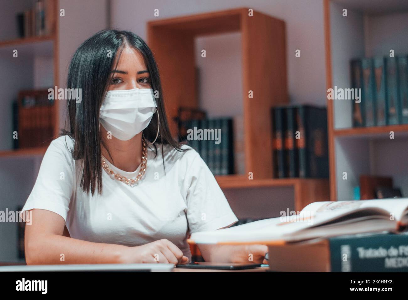 Eine spanische, junge Frau mit einer Gesichtsmaske, die in der Bibliothek studiert Stockfoto