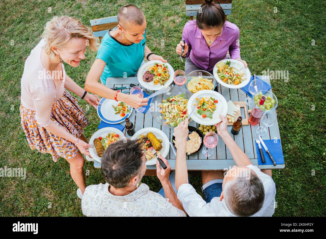 Blick aus dem hohen Winkel auf Erwachsene Freunde, die zusammen am Tisch sitzen und Essen auf Teller legen, während sie im Hinterhof ein Feiertagsessen machen Stockfoto