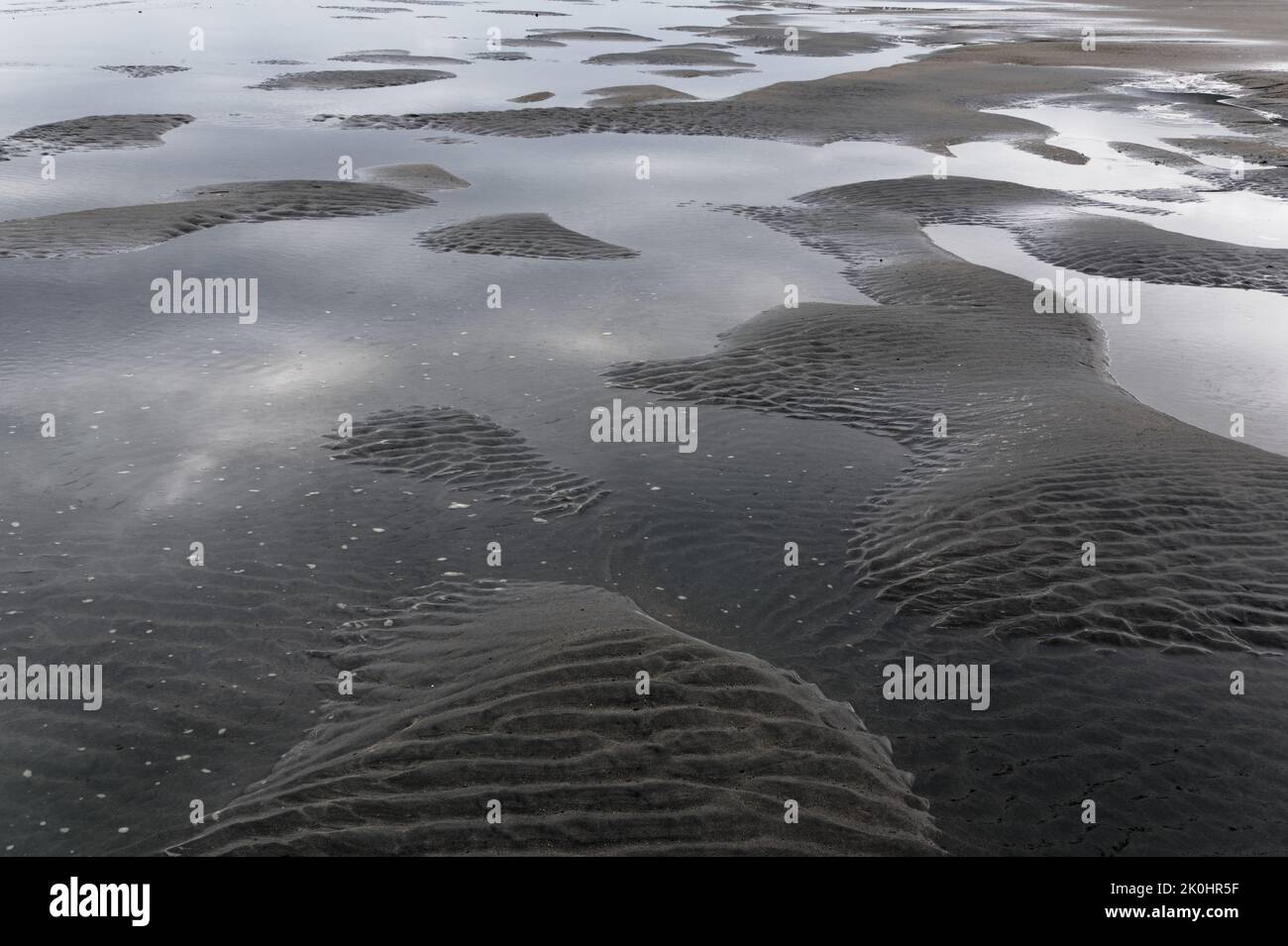 Die ausgehende Flut hat eine Reihe von Höckern und Mulden hinterlassen, die den Sand umhergewellt haben und Sandinseln, die von Wasserbecken umgeben sind, hinterlassen. Stockfoto