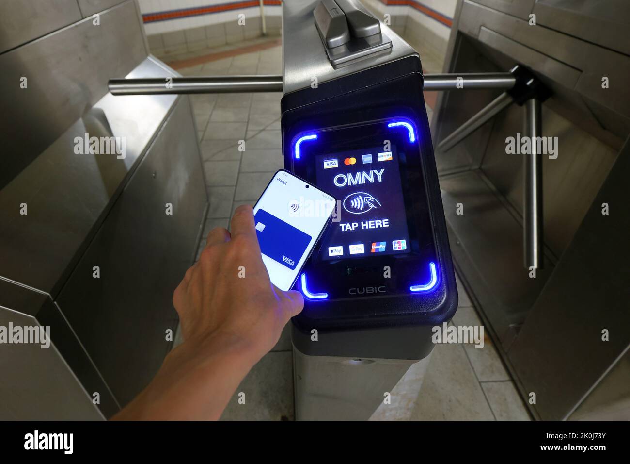 Ein Smartphone mit Google Wallet tippt auf eine NYC U-Bahn-Drehkreuze, die mit einem OMNY kontaktlosen Bezahlleser ausgestattet ist, der NFC-Zahlungen akzeptiert Stockfoto