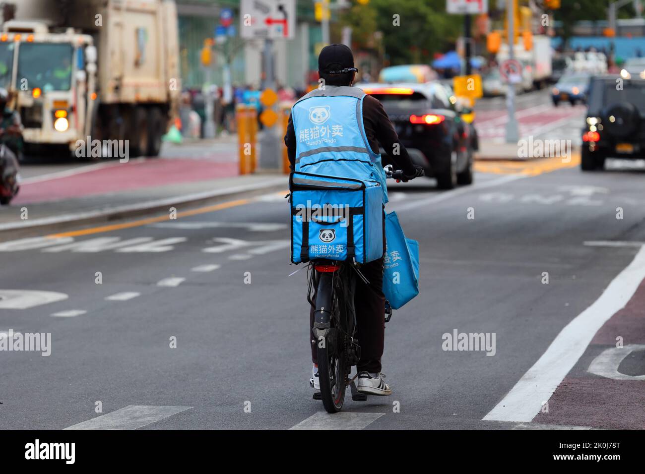 Eine Person, die Lebensmittel von HungryPanda auf einem E-Bike in Downtown Flushing, New York, geliefert hat. Hungry Panda 熊貓外賣 Lieferung asiatischer Lebensmittel. Stockfoto