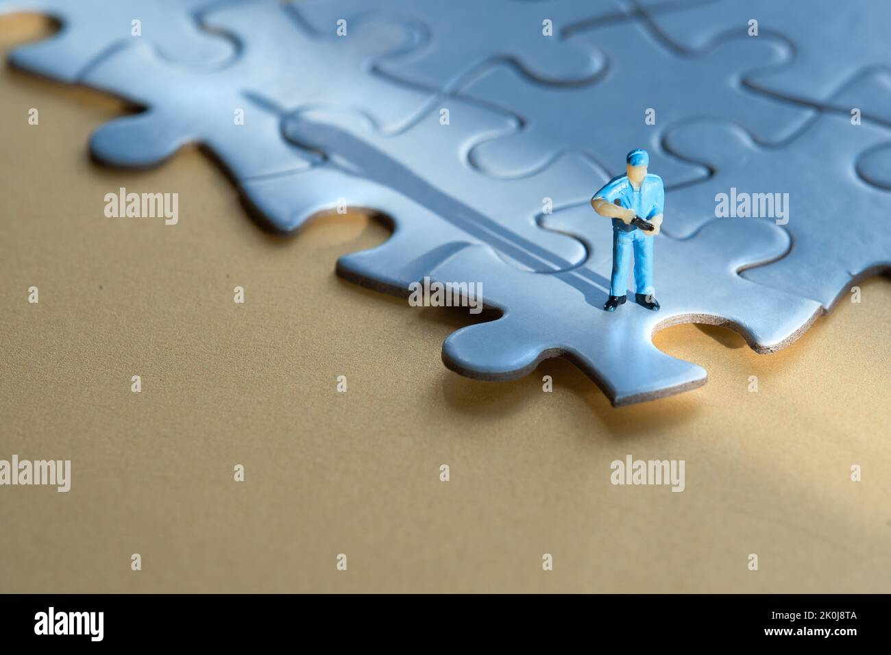 Einzelne kleine Arbeiter Miniatur-Figur am Rand des verknüpften blauen Puzzle. Gelber Papierhintergrund, langer Schatten. Konzept-Hintergrund mit Copy-Space Stockfoto