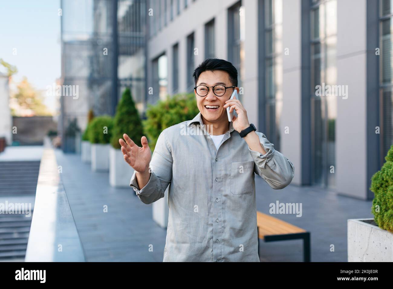 Glücklicher erfolgreicher asiatischer Geschäftsmann im Gespräch auf dem Smartphone, im Freien stehend gegen modernes Bürozentrum, freien Raum Stockfoto