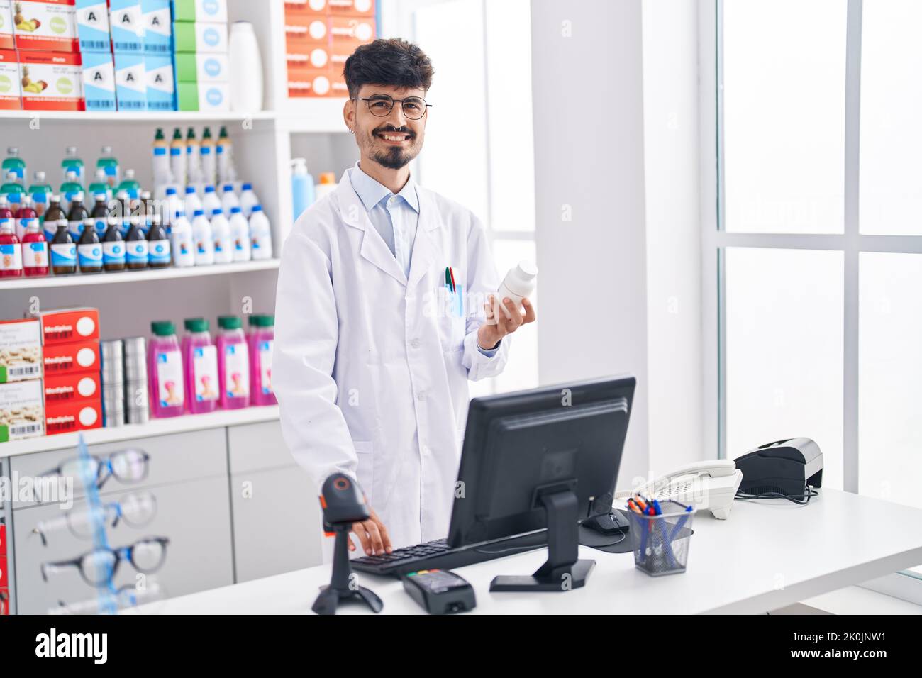Junger hispanic Mann Apotheker hält Pillen Flasche mit Computer in der Apotheke Stockfoto