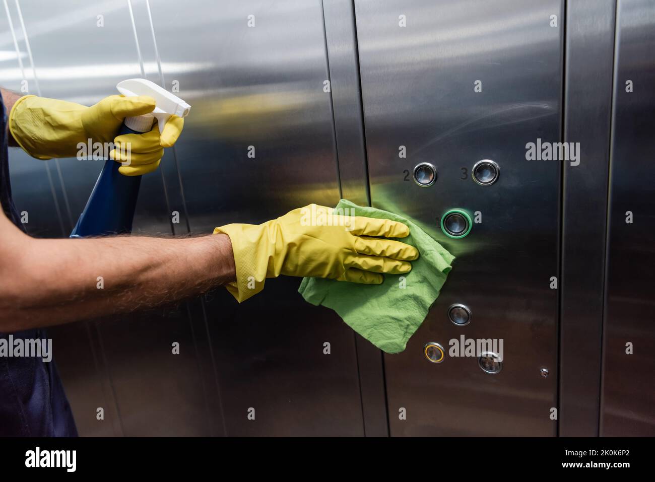 Teilansicht des Mannes in Gummihandschuhen, der den metallischen Aufzug reinigt, Stockbild Stockfoto