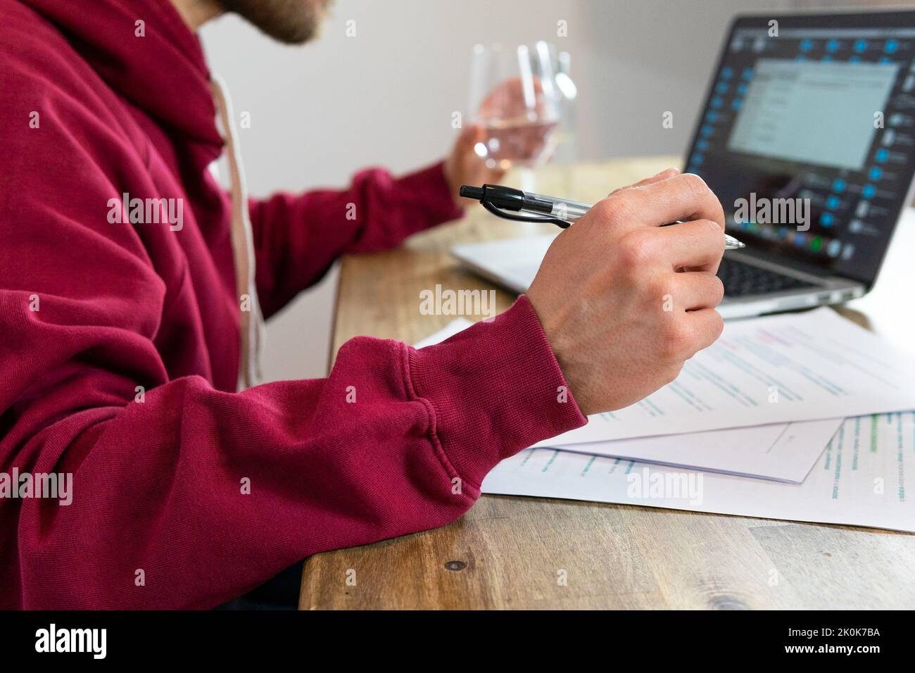 Nicht erkennbarer männlicher Arbeiter, der im Netbook im Internet surft und während der Arbeit im Lichtbüro mit einem Glas Wasser am Schreibtisch sitzt Stockfoto