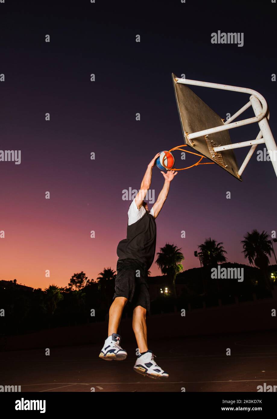 Basketballspieler in schwarz-weißen Sportkleidung springen und machen Dunk beim Training auf Sportplatz Stockfoto