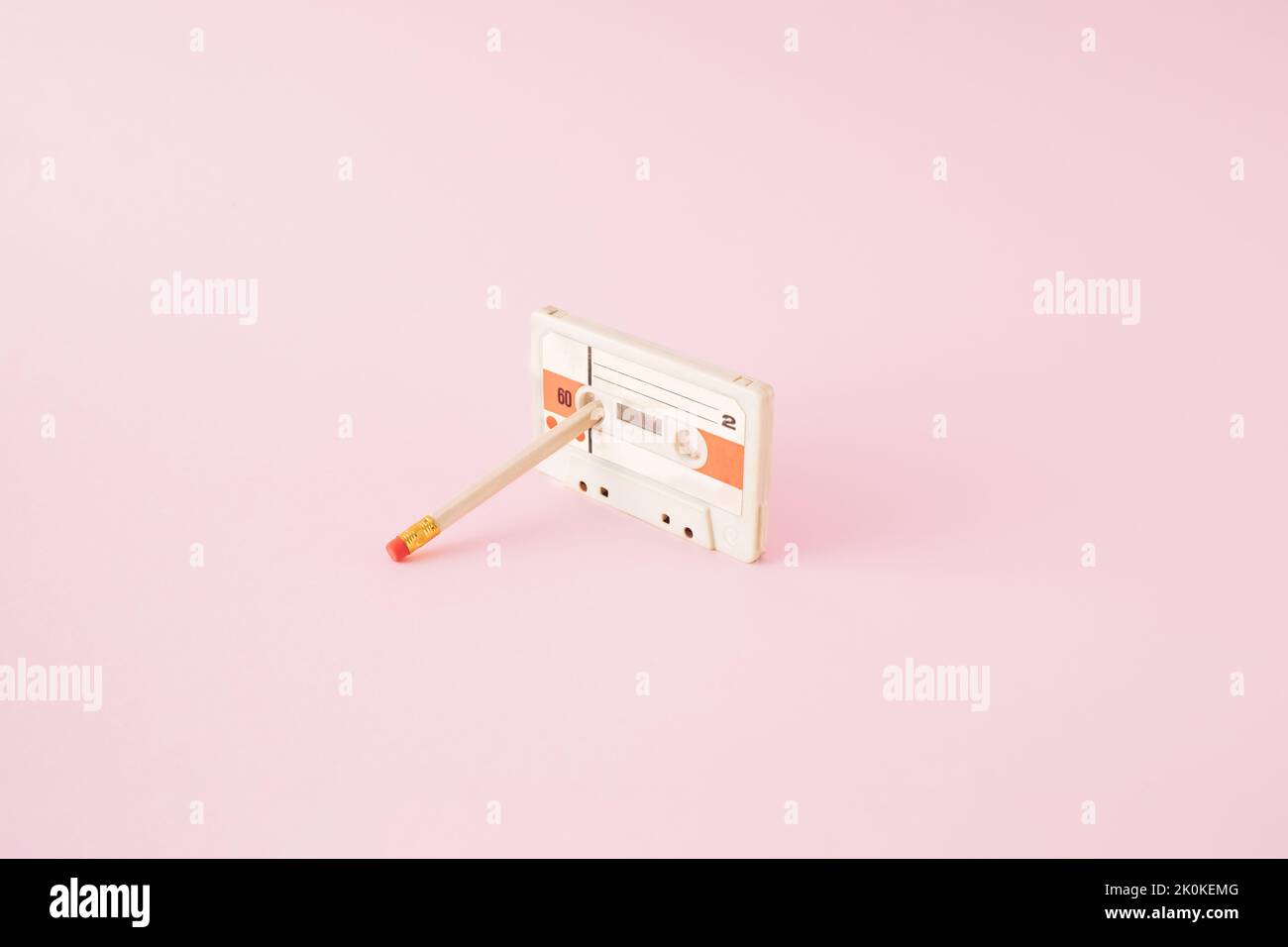 Retro-Audiokassette mit Bleistift, der auf einem rosafarbenen Hintergrund in einer Rolle geklebt ist. Stockfoto
