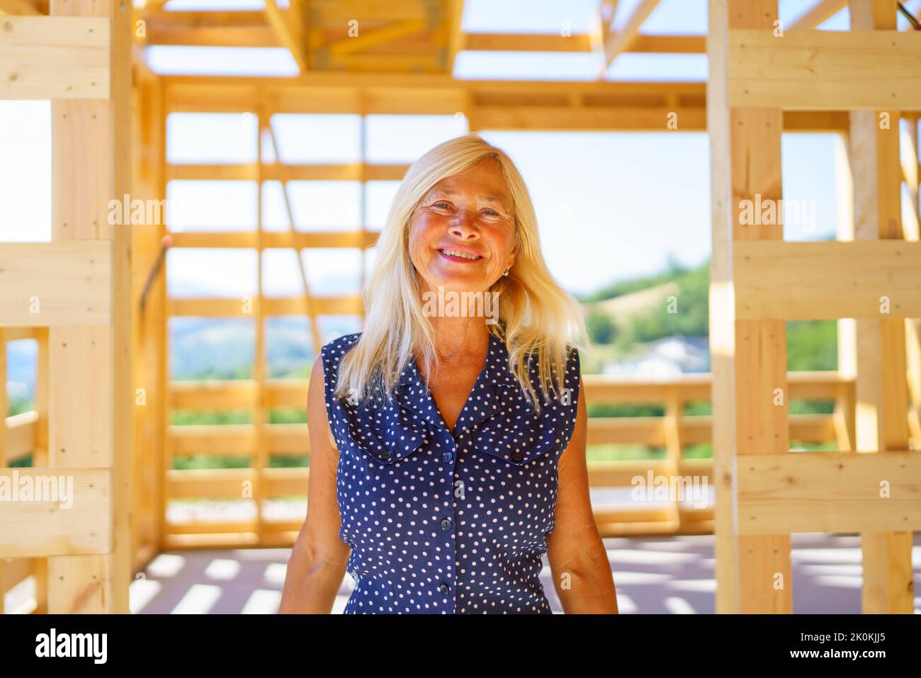 Glückliche ältere Frau in ihrem neuen unfertigen ökologischen Holzhaus. Stockfoto