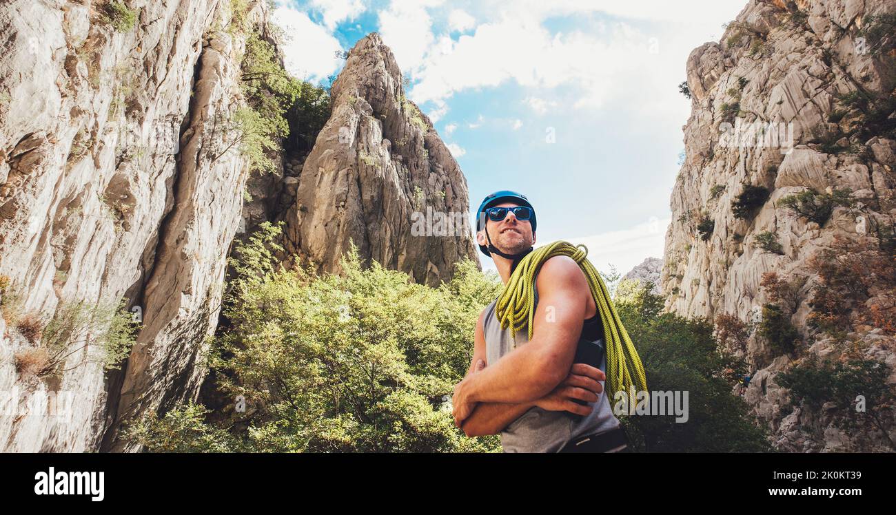 Porträt eines lächelnden Kletterers Mann in Schutzhelm und Sonnenbrille mit Kletterseil auf der Schulter stehend im Paklenica Park zwischen Felsklippe w Stockfoto