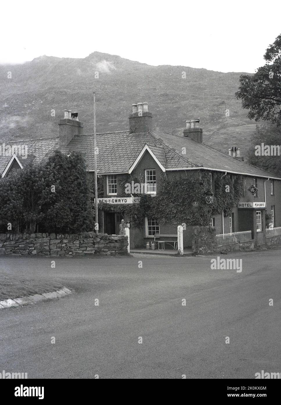 1956, historisch, ein Gentleman, der vor dem Eingang zum Pen-y-Gwryd Hotel, Nant Gwynant, Caernarfon, Wales, Großbritannien steht. Es liegt in einem Tal in Snowdonia und wurde 1810 erbaut und später zu einem gasthaus für Wanderer und Kletterer, die Snowdonia besuchen. Im Jahr 1953 war es Sir Edmund Hillary Trainingsbasis vor seiner erfolgreichen Mount Everest-Besteigung. Stockfoto