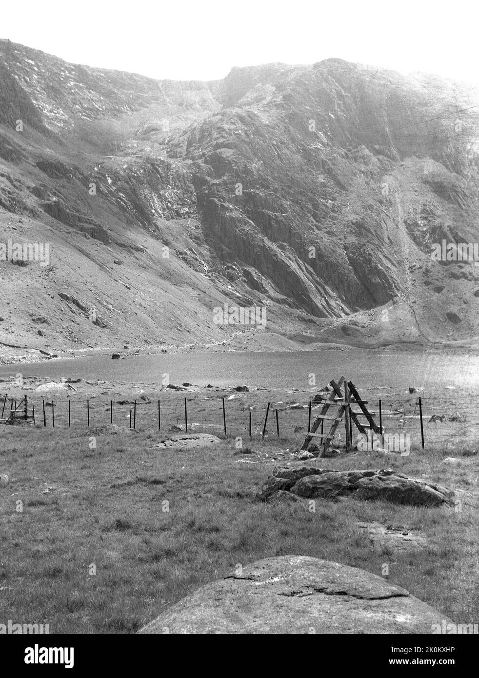 1956, historisch, ein Holzstiel in einem Feld, Berge im Hintergrund, Snowdonia, Wales, Großbritannien. Stile sind Bauwerke, die oft mit Stufen oder Leitern in ländlichen Gebieten gebaut werden, die es Spaziergängern ermöglichen, über einen Zaun zu gehen, während sie den Tieren Schutz bieten und ihnen das Entweichen verhindern. Stockfoto