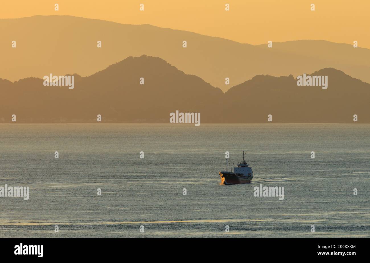 Frachtschiff segelt vor der Bergküste mit orangefarbenem Sonnenuntergang Stockfoto