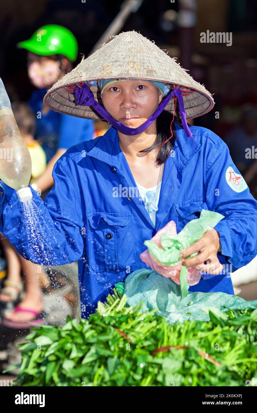 Vietnamesischer Anbieter mit Bambushut, der auf dem Straßenmarkt unter freiem Himmel arbeitet, Bewässerung von Pflanzen, Hai Phong, Vietnam Stockfoto