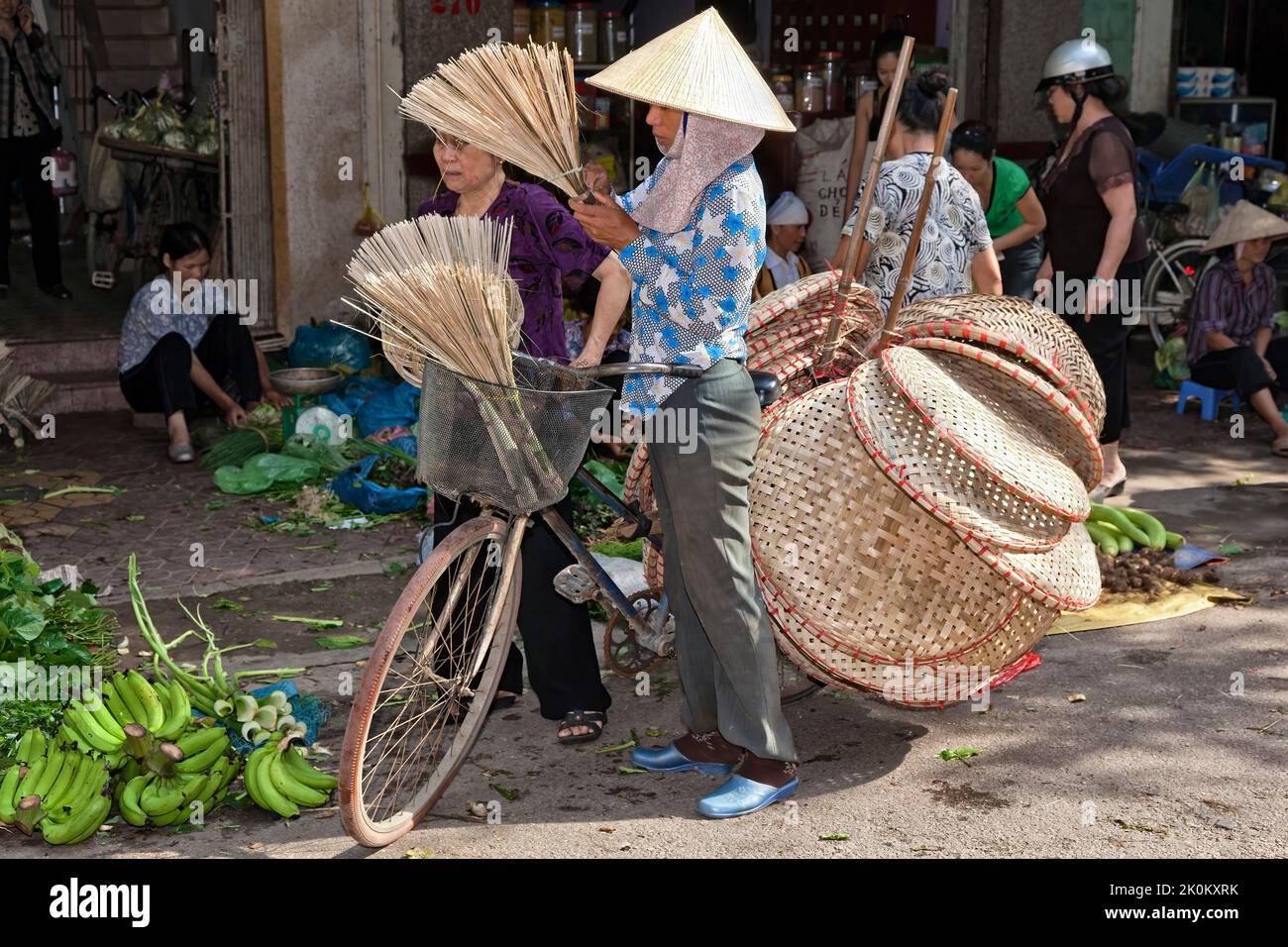 Vietnamesischer Händler mit Bambushut, der Korbartikel vom Fahrrad verkauft, arbeitet auf dem Straßenmarkt im Freien, Hai Phong, Vietnam Stockfoto