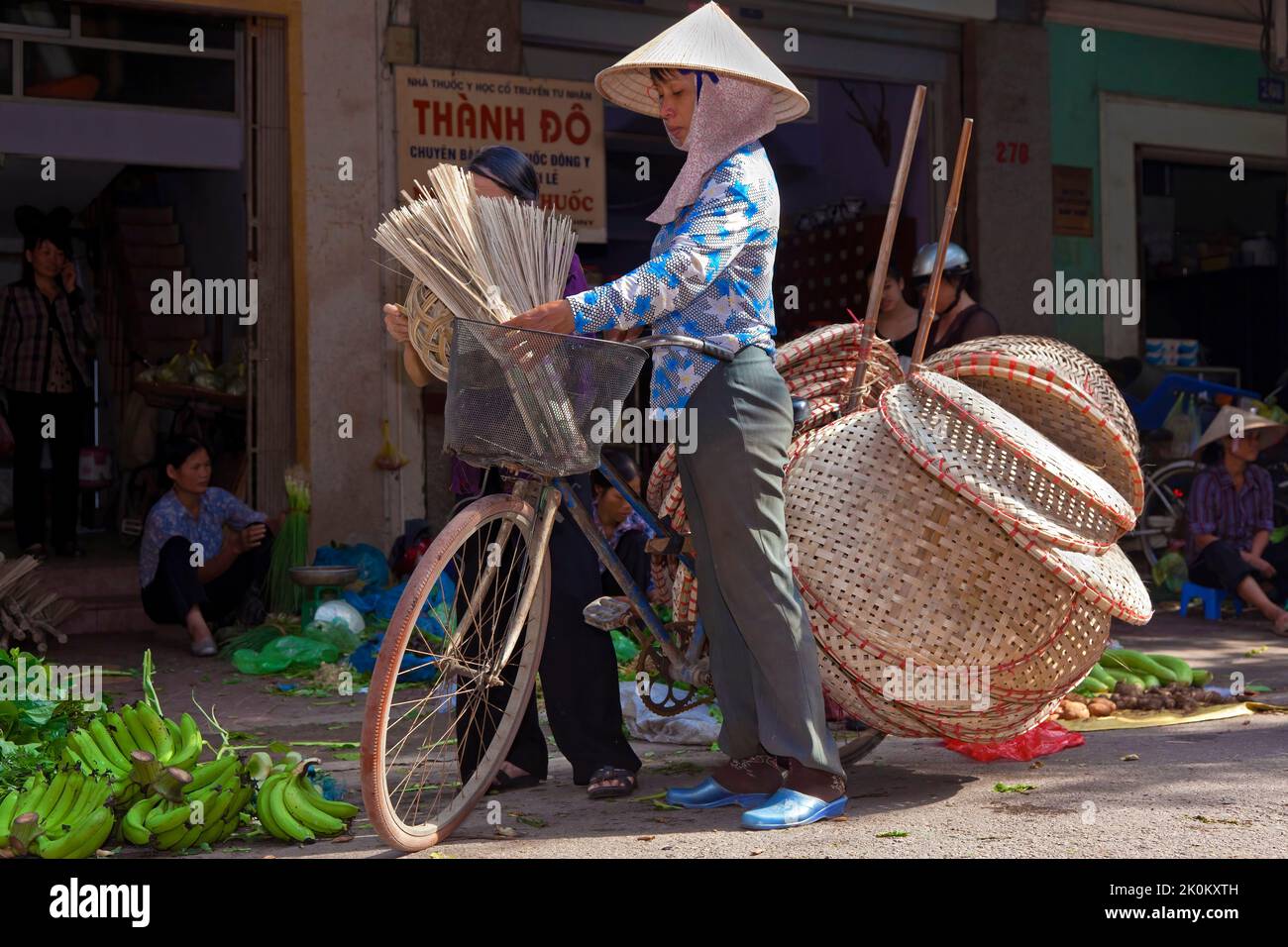 Vietnamesischer Händler mit Bambushut, der Korbartikel vom Fahrrad verkauft, arbeitet auf dem Straßenmarkt im Freien, Hai Phong, Vietnam Stockfoto