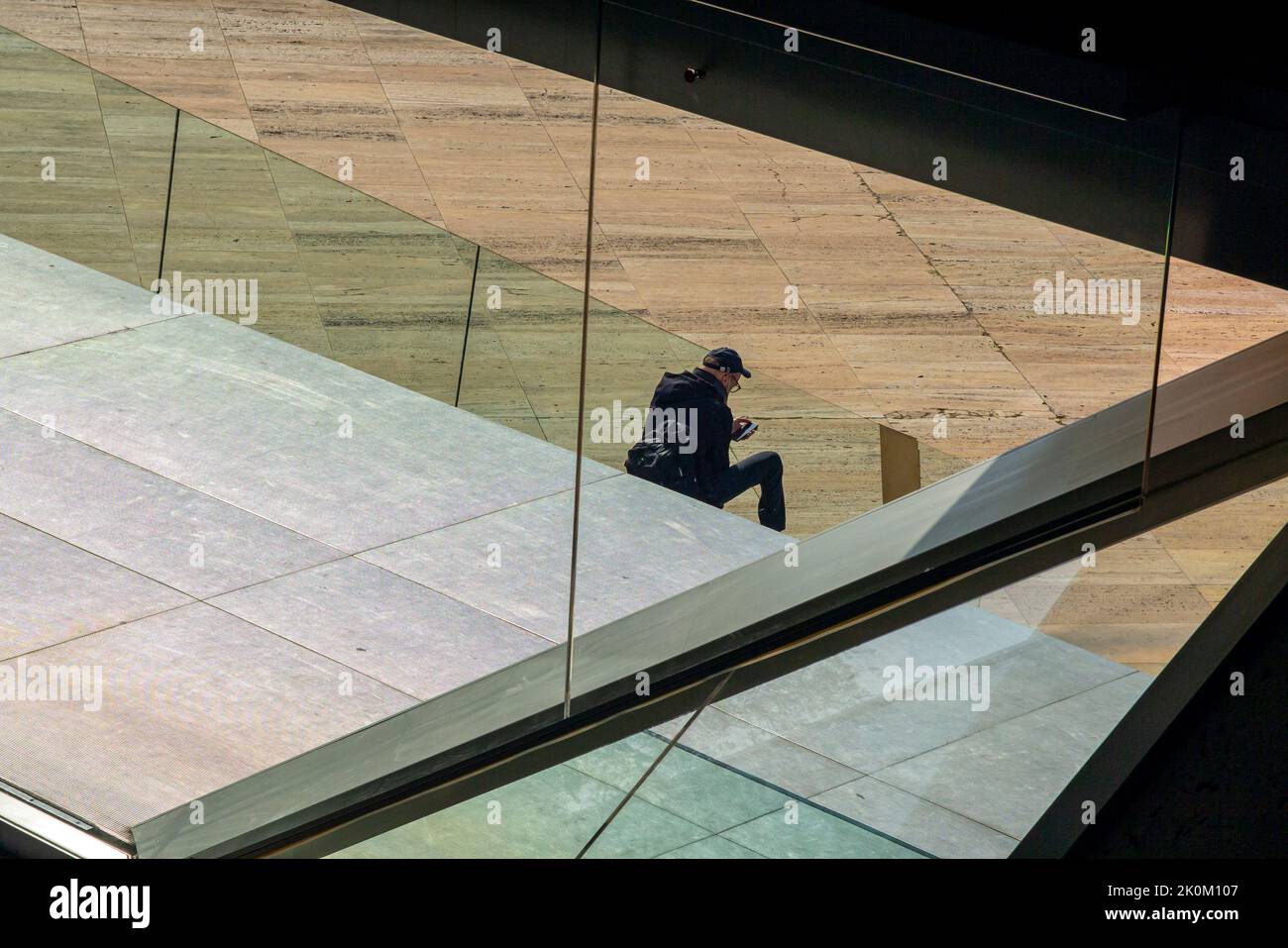 Ein Mann, der durch das Fenster eines modernen Gebäudes auf das Mobiltelefon schaute. Stockfoto