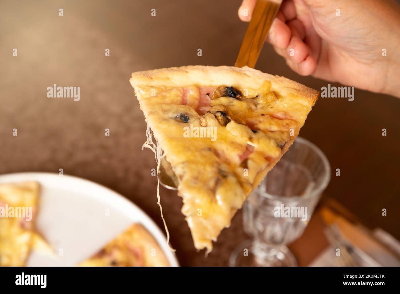 Scheibe Pizza mit Schinken, Pilzen und Käse auf einem Servierspatel und einer Männerhand. Nahaufnahme, Sonnenauffackel Stockfoto