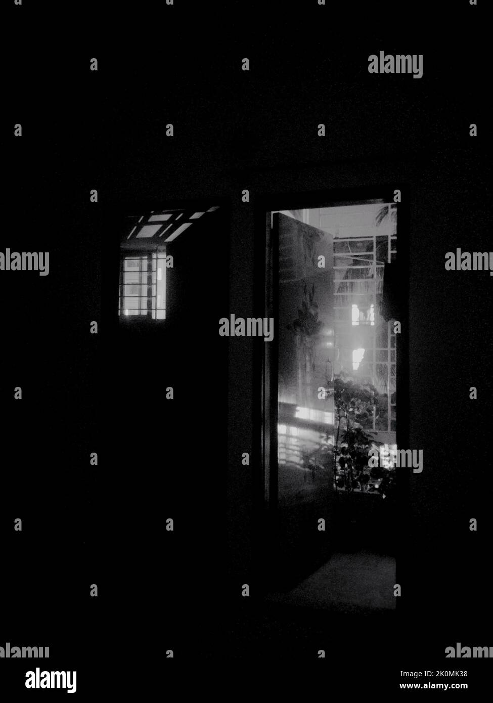 Eine vertikale Graustufenaufnahme aus einem dunklen Raum mit einer offenen Tür und einem Fenster Stockfoto
