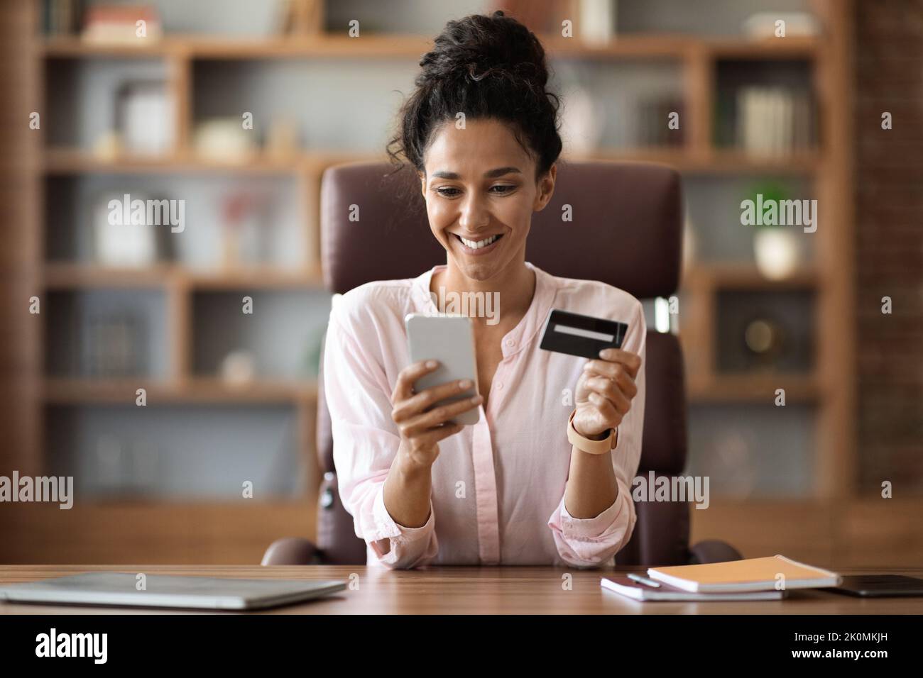 Positive Geschäftsfrau, die online im Büro mit dem Smartphone einkauft Stockfoto