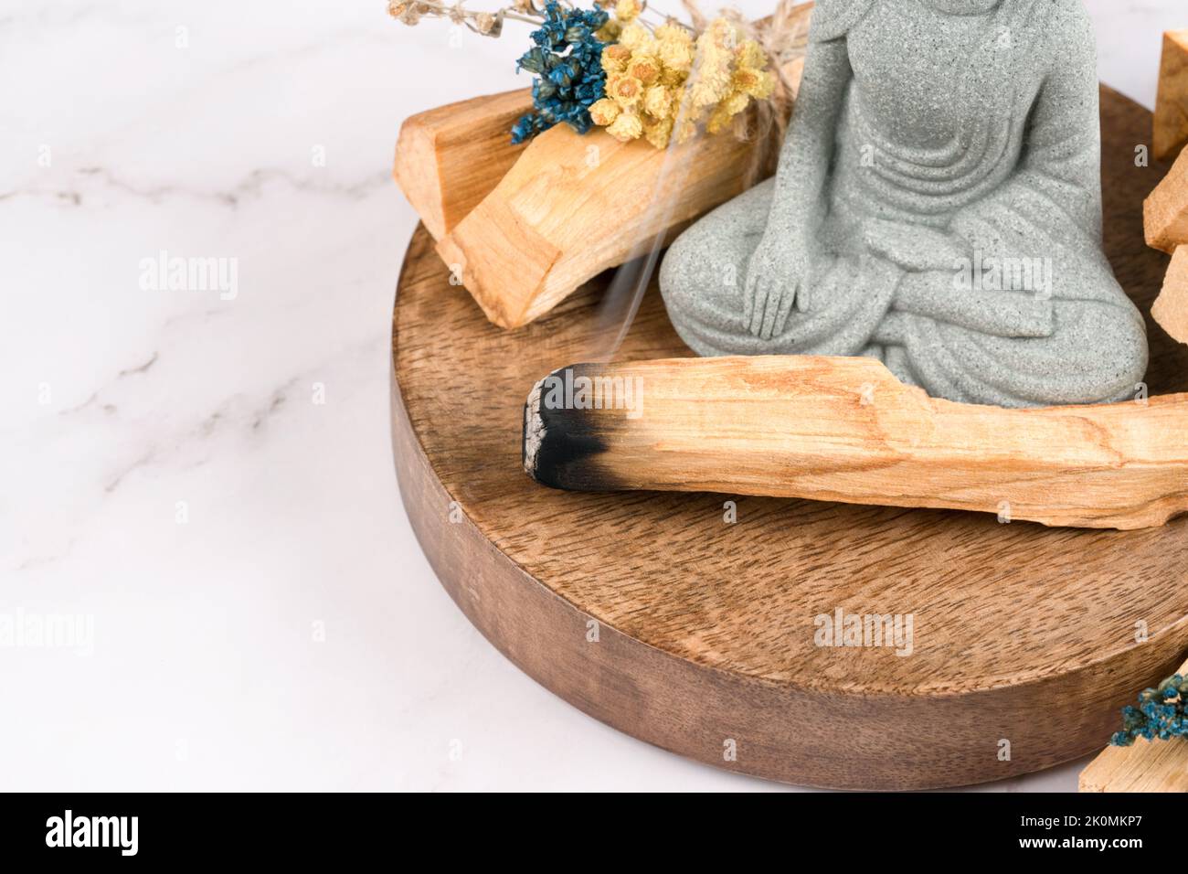 Verschmieren mit palo santo-Stäbchen und Buddha-Statue auf weißem Marmortisch. Raumbegasungsritual für Meditation und spirituelle Praktiken. Burnin für Räucherstäbchen Stockfoto