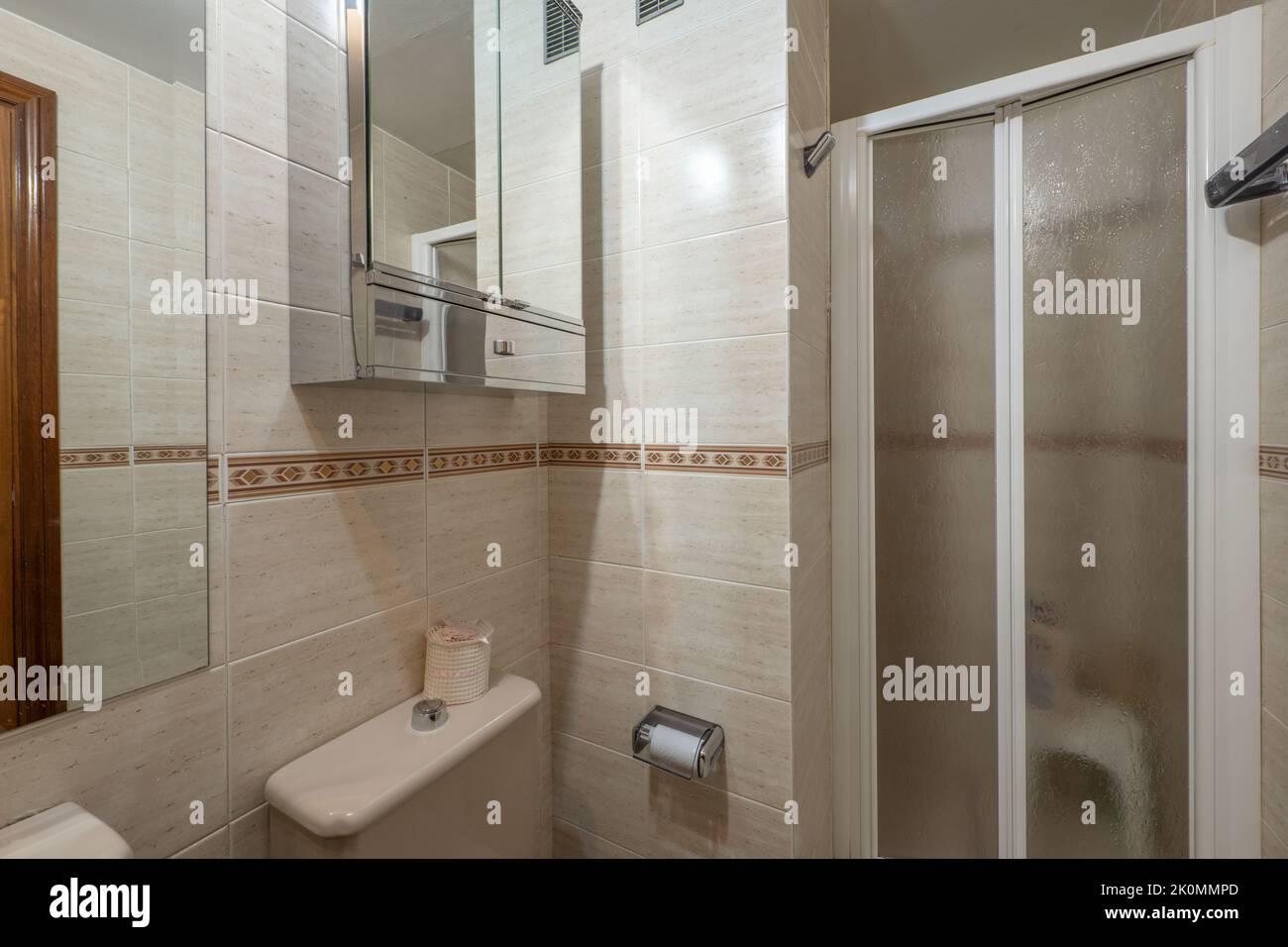Bad mit weißen Porzellanarmaturen, rahmenlosem Spiegel an der Wand und quadratischer, begehbarer Dusche mit Doppelscheibe Stockfoto