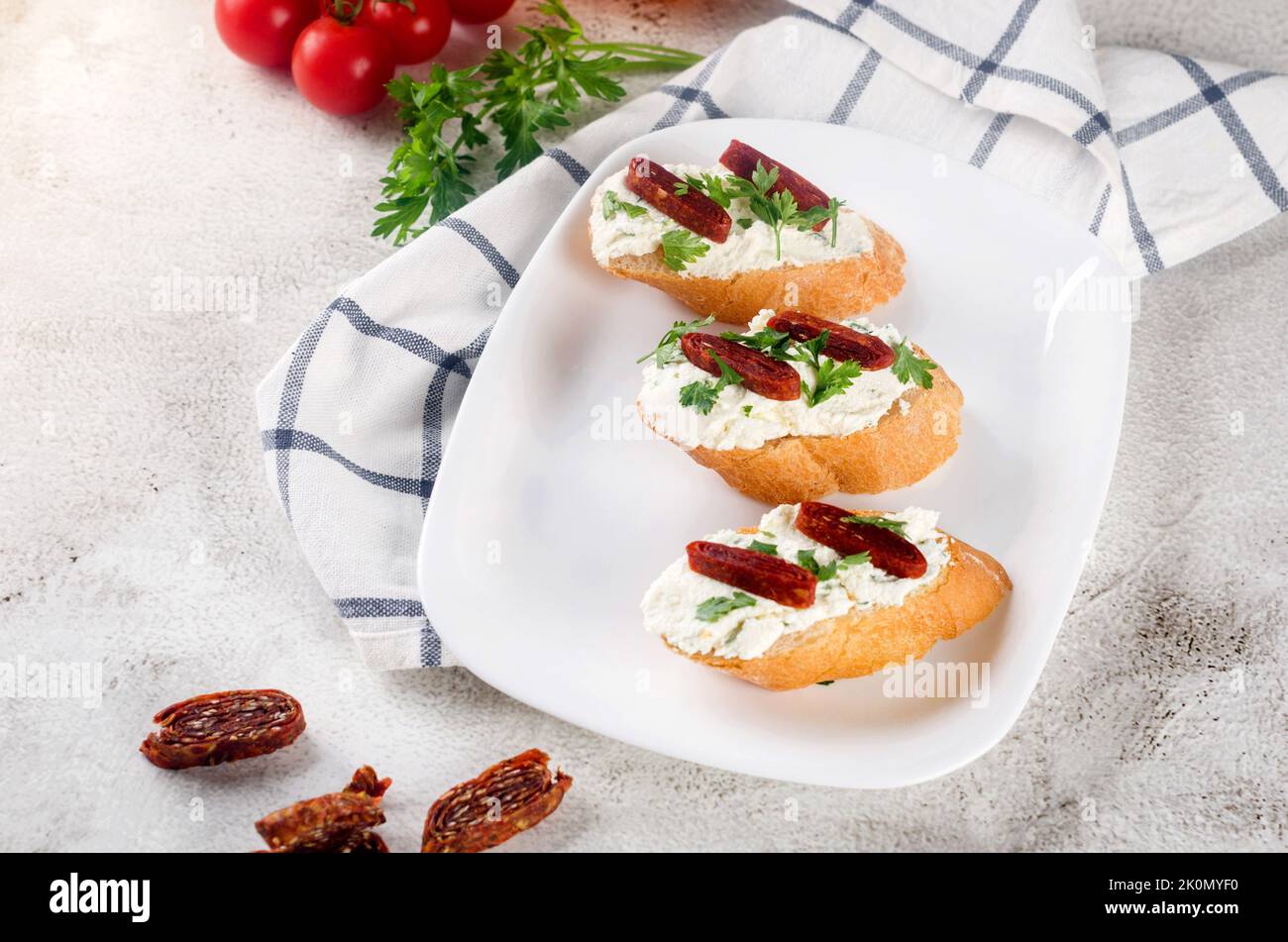 CANape oder Crostini mit geröstetem Baguette, Frischkäse, sonnengetrockneten Tomaten, Kräutern auf weißem Teller. Handgemachte leckere Sandwiches zum Frühstück. Stockfoto