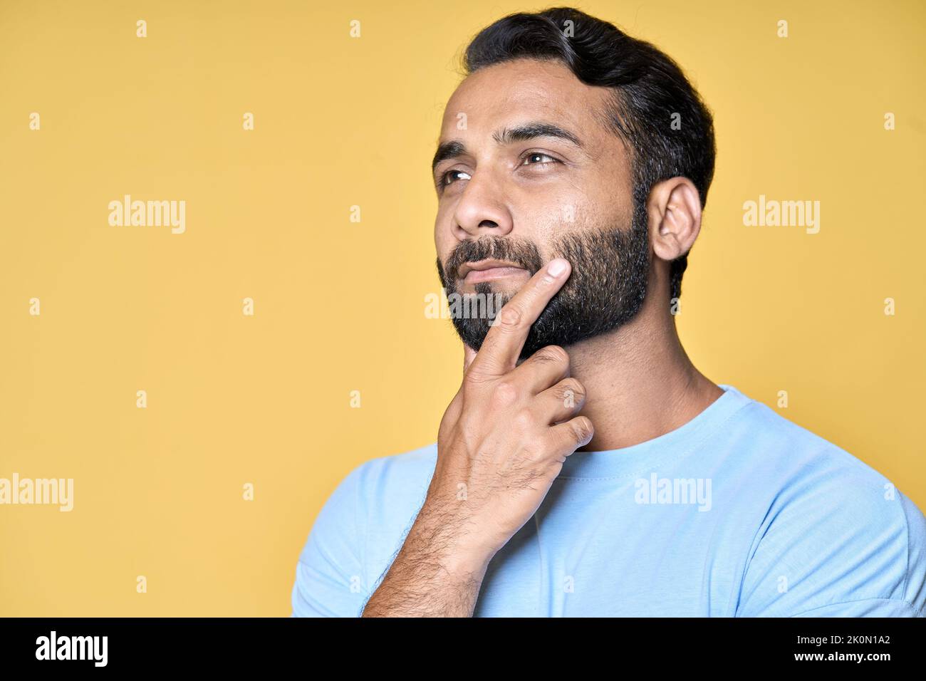 Nachdenklicher bärtiger indischer Mann, der isoliert auf gelbem Hintergrund zur Seite schaut. Stockfoto