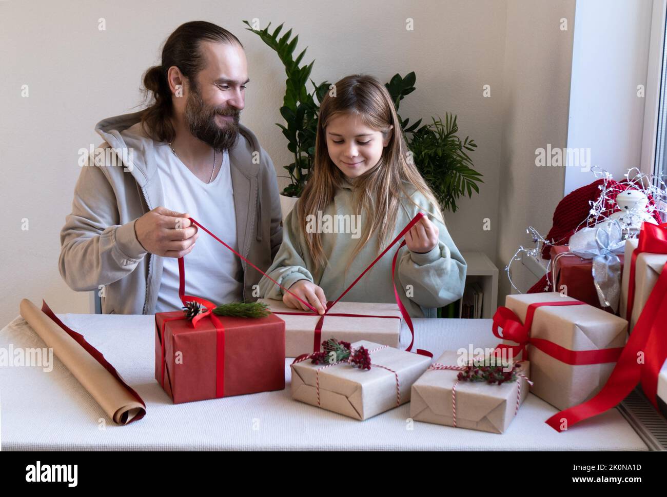 Frohe Weihnachten und frohe Feiertage. Fröhlicher Vater und Tochter packen Öko-Geschenke für die ganze Familie. Das Konzept der Vorbereitung auf den Urlaub mit der ganzen Familie zu Hause. Vorderansicht zu Hause. Stockfoto
